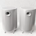 Two White Cylindrical Speakers With Round Speaker Holes And Small Feet At Bottom