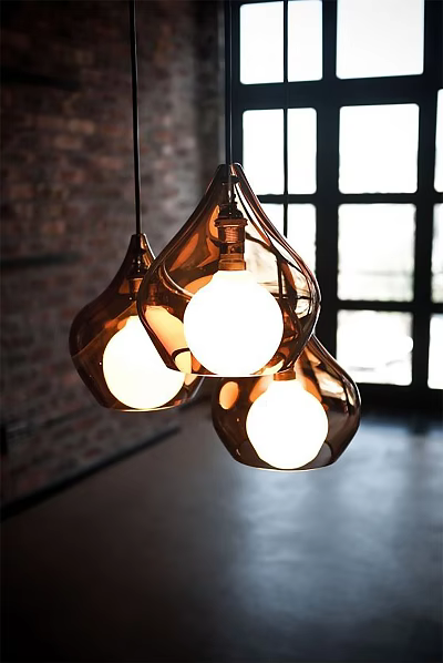 Three Amber Glass Teardrop Pendant Lights Hanging In Bright Interior With Brick Wall 3d model