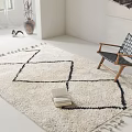Ivory Square Rug With Black Geometric Pattern And Tassels Next To Woven Chair In Living Space