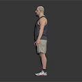 Man With Arm Tattoo Wearing Gray Tank Top Khaki Shorts Sneakers Standing Against Dark Background