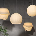 Cream Colored Paper Pendant Lights With Unique Designs Hanging On Gray Wall And Green Plant