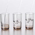 Three Transparent Glass Cups With Brown Base As Water Splashes In