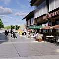 Vibrant Commercial Street With Outdoor Seating Green Umbrellas And Pedestrians Walking