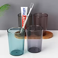 Daily Washing Essentials With Colorful Glass Cups Toothpaste Toothbrush And Green Leaves On Wooden Tray