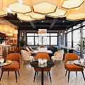 Modern Café Interior With Blue Sofa Orange Chairs Round Tables Pendant Lights And Green Plants