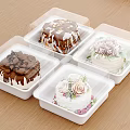 Four Assorted Decorated Cakes in White Plastic Containers on Wooden Table