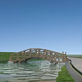Wooden Arch Bridge Over Water With Green Grass And Paved Path Under Blue Sky