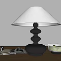 Black Table Lamp with White Lampshade Open Book Camera and Moss Container on Wooden Table