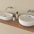 Oval And Round White Washbasins On Wooden Countertop With Wall Mounted Faucets And Soap Dispensers