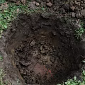 Garden Landscape Excavated Hole Surrounded by Soil Stones and Green Grass on Ground