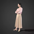 Woman in pink top and beige long skirt with crossed arms standing against gray background