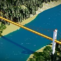 Red Suspension Bridge With White Towers Over Blue River By Green Forest