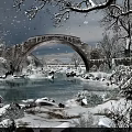 Gorgeous Snowy Winter Landscape With Ancient Stone Arch Bridge Over Calm River And Falling Snowflakes