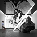 Black Stone Sculpture With White Lines Against Tree Patterns Background And Person Walking Nearby