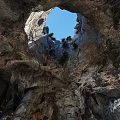 Natural Cave Interior Featuring Rock Formations Ancient Humans Campfire Sunlight Through Entrance And Green Plants