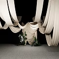 Stylish Floral Display Featuring White Draped Fabric And Central Decorative Greenery On Gray Floor