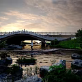Scenic Stone Arch Bridge With White Railing Over River Rocks And Trees Under Sunset Sky