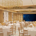 Modern Banquet Hall Featuring Round Tables Chairs White Tablecloths Yellow Flowers Large Screen Gold Chandeliers
