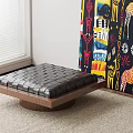 Black Leather Ottoman With Diamond Stitching And Wooden Base On Carpet Near Colorful Abstract Painting