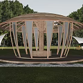 Circular Wooden Gazebo With Open Framework Supporting Columns On Green Lawn Surrounded By Trees