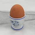Fresh Brown Egg in Blue and White Patterned Egg Cup on Light Colored Surface 3d model