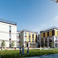 Modern School Building Exterior With White Yellow Facade Green Lawn And Children Playing
