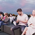 Group of People Relaxing Outdoor Evening Sitting on Benches with Sunset Sky and Smartphones