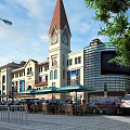 Vibrant Commercial Street With Clock Tower Outdoor Seating Green Umbrellas And Trees