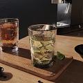 Two Glasses With Brown Liquid And Green Drink Lime On Wooden Tray Near Coffee Machine