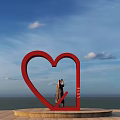 Red Heart Sculpture With LOVE Letters And Person Taking Photo Against Blue Sky And Sea