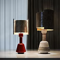 Two Modern Table Lamps With Red And Textured Bases And Metallic Shades On Light Table