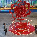 Giant Red Rose Sculpture Illuminated At Night With City Skyline And People Around