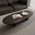 Modern Black Oval Coffee Table With Open Magazine White Tray Glass Cups Near Gray Sofa