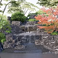 Rockery Stones With Waterfall Red Maple And Lush Greenery In Garden Landscape