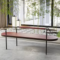 Modern Maroon Sofa Bench With Black Metal Legs Bamboo Plants Stone Pebbles And Large Windows