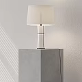 Modern Illuminated Table Lamp With White Lampshade On Gray Cubic Base Against Light Wall Background