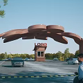 Unique Architectural Entrance Gate With Security Booth Cars People And Green Trees Background