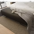 Black Footstool With Plaid Blanket Beside Bed On Wooden Floor And Woven Rug