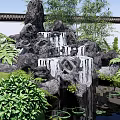 Rockery Stones With Waterfall In Garden Pond Surrounded By Green Plants And Lotus Leaves