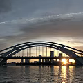 Modern Bridge Sunset View With Sun Behind Distant City Skyline And Water Reflection