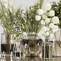 Transparent Vases With White Pompom Flowers Green Leaves And Wheat Like Plants In Light Background