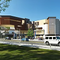 Modern Commercial Complex Exterior With Pedestrians Vehicles And Greenery Along Street