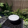 Tranquil Garden Landscape Featuring Circular Water Fountain Lush Green Plants Bamboo Fence And Pebbles