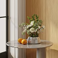 Silver Vase With White Flowers And Green Foliage On Round Marble Table With Oranges