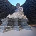 White Buddha Sculpture Seated On Lotus Pedestal Against Curved Black Building Blue Sky