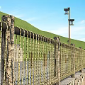 Metal Woven Fence Along Stone Path With Green Hills And Street Lights