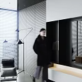 Woman in dark coat with blurry back near black floor lamp and grey striped wall