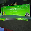 Large Conference Venue With Green Stage Speaker Red White Chairs And Big Screen