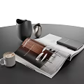 Decorative Ornament Set with Black Jug Silver Cup Open Magazine Coffee Latte Art on Tabletop