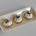 Three Golden Shell Tarts With White Cream And Black Sprinkles On White Rectangular Tray 3d model